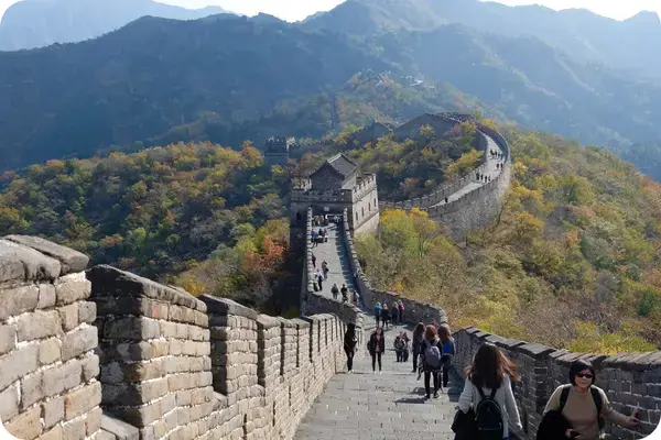 Turistas sobem os degraus da Muralha da China entre montanhas com folhagem de outono