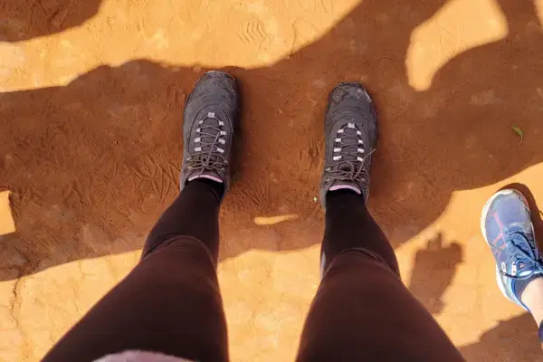 Botas de trekking em solo de terra vermelha durante trilha no Brasil