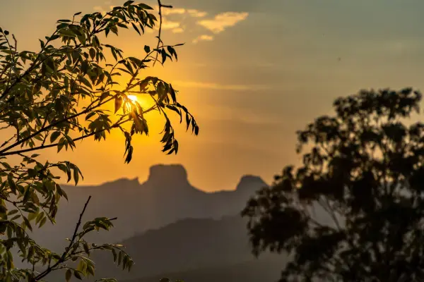 Vista da Pedra do Baú ao amanhecer com silhueta de árvores e céu alaranjado em São Paulo