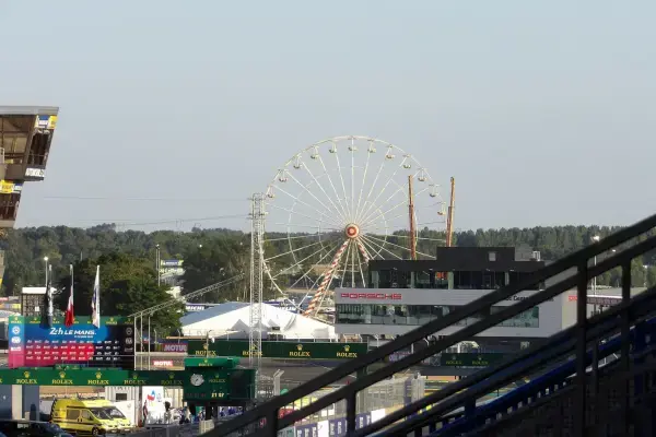 Vista panorâmica do Circuit de la Sarthe durante as 24 Horas de Le Mans, com roda-gigante, paddock e estruturas do evento ao fundo.