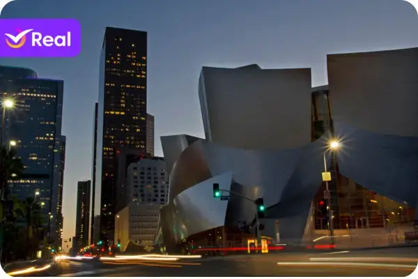 Fachada do Walt Disney Concert Hall em Downtown Los Angeles, mostrando suas curvas de aço inoxidável sob um céu azul, com os arranha-céus da cidade ao fundo.
