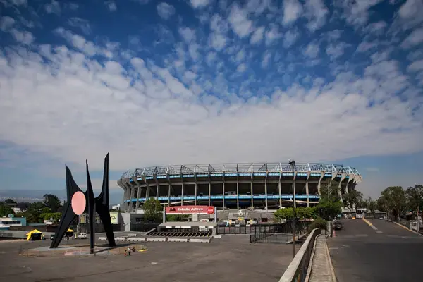 Vista externa do Estadio Azteca, na Cidade do México, durante o dia, com céu azul e área ao redor.