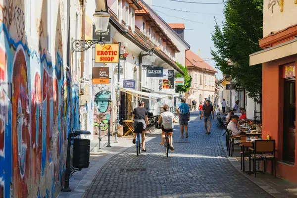 Ciclistas em rua de paralelepípedos com grafites e cafés em Ljubljana