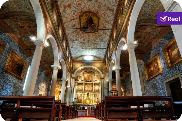 Nave da Igreja Matriz de Santa Maria de Óbidos, destacando a arquitetura maneirista, o teto com pinturas de brutesco do século XVII e as paredes revestidas por azulejos barrocos azuis e brancos. Ao fundo, vê-se o retábulo-mor em talha dourada.