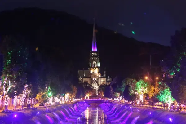 Catedral São Pedro de Alcântara em Petrópolis iluminada para o Natal, vista ao fundo de rio com árvores decoradas.