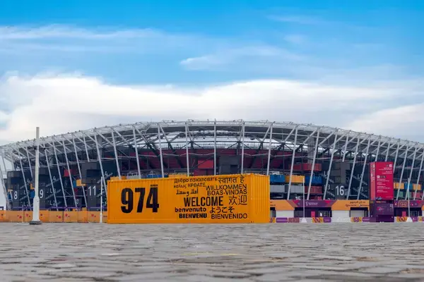 Vista externa do Estádio 974 no Catar, com fachada metálica circular ao fundo e estrutura amarela com o número 974 em destaque na entrada, exemplo de arena modular da Copa do Mundo 2022.