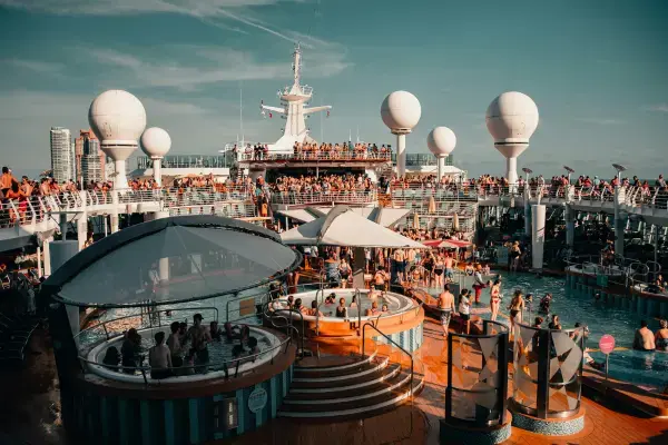 Deck superior de navio de cruzeiro lotado, com piscinas, hidromassagens e pessoas ao sol
