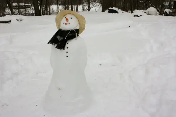 Boneco de neve com chapéu de palha e cachecol preto.