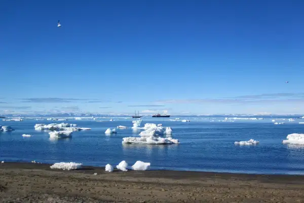 praia com o mar coberto de gelo por cima, ao fundo pequenos navios