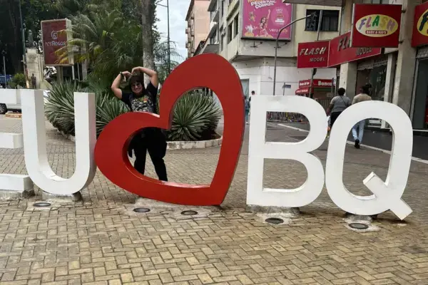 Pessoa posando no letreiro “Eu amo BQ” no centro de Barbacena.