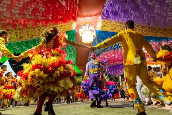 Dançarinos de quadrilha junina com roupas coloridas girando sob bandeirinhas