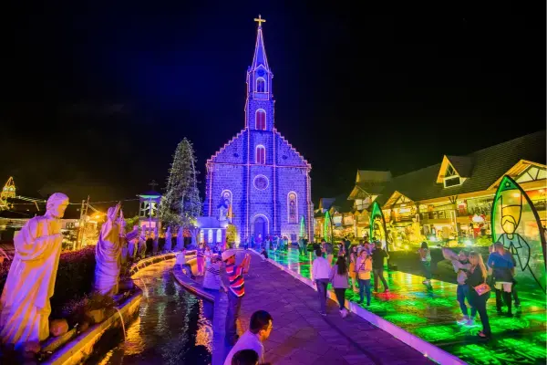 Igreja matriz de Gramado iluminada durante o Natal, com visitantes caminhando pela área decorada à noite.