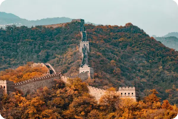 Muralha da China serpenteando por montanhas cobertas de folhagem alaranjada no outono