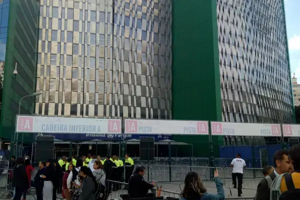 Foto da entrada do Allianz Parque, em São Paulo, com fãs na fila, seguranças organizando o acesso e placas indicando setores de pista e cadeiras.