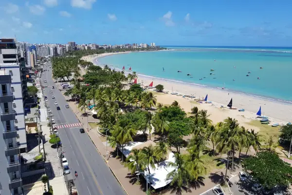 Vista aérea da orla de Maceió com coqueiros, areia branca e mar verde-esmeralda