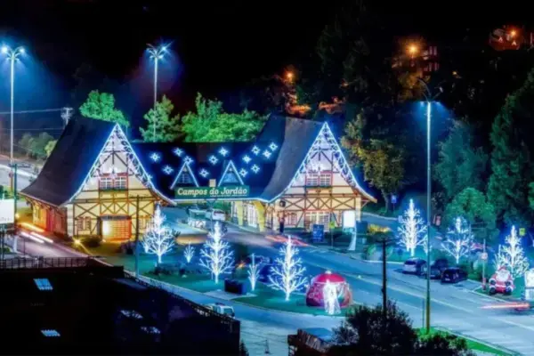 Portal de entrada de Campos do Jordão iluminado durante a temporada de Natal, com árvores decoradas e luzes azuis ao longo da avenida à noite.