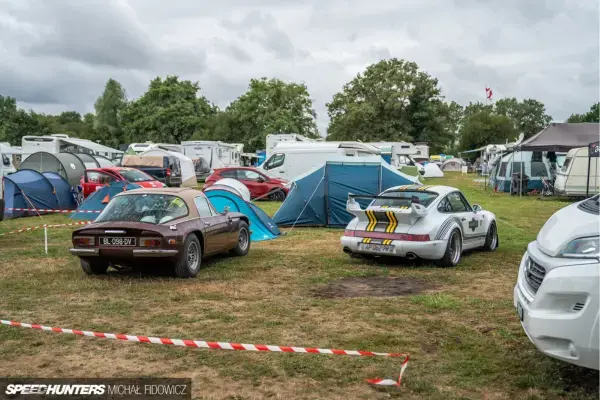 Área de camping oficial nas 24 Horas de Le Mans, com barracas, motorhomes e carros clássicos próximos ao circuito.
