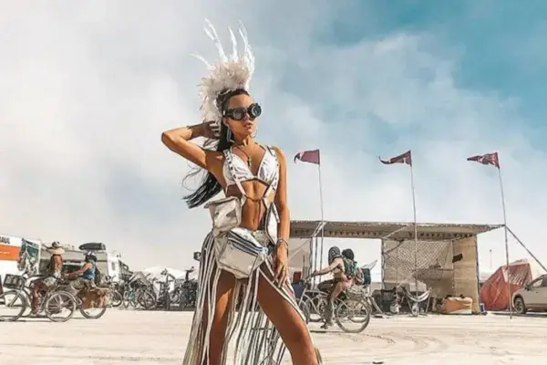 Mulher com look elaborado de headpiece de penas e roupa prateada no Playa do Burning Man