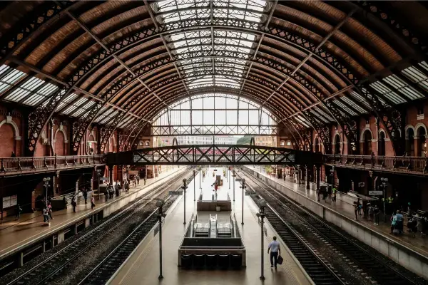Interior da Estação da Luz em São Paulo, com plataformas de trem, cobertura metálica e pessoas circulando durante o dia.
