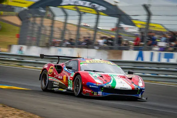Ferrari GT número 51 em alta velocidade durante as 24 Horas de Le Mans, passando por área cercada do circuito com público ao fundo.