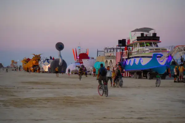 Participantes de bicicleta ao lado de mutant vehicles no Playa do Burning Man ao entardecer