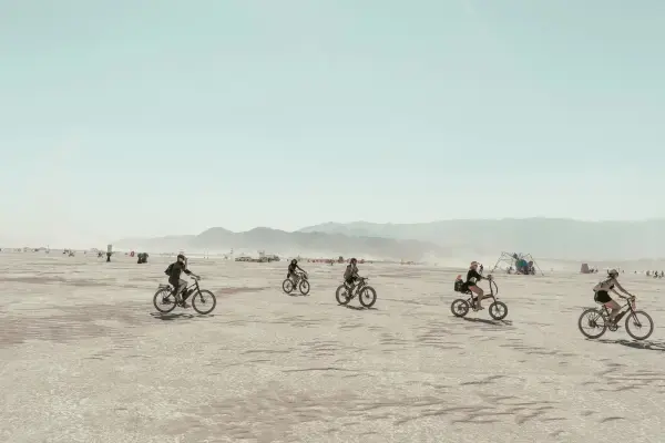Grupo de participantes pedalando no vasto deserto do Burning Man com montanhas ao fundo