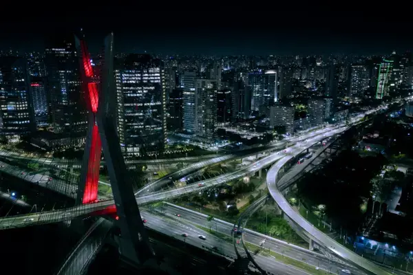 Vista aérea noturna da Ponte Estaiada Octávio Frias de Oliveira, em São Paulo, com vias iluminadas e prédios ao redor.