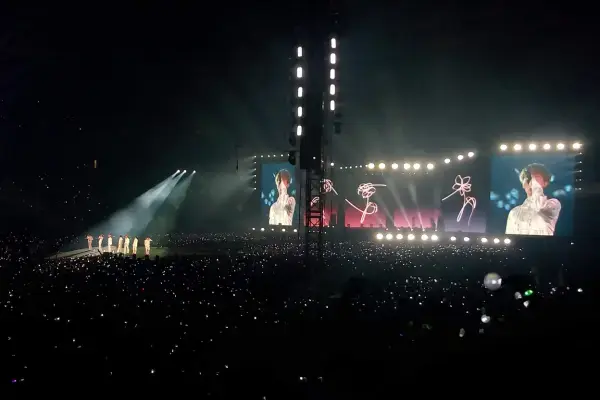Foto de um estádio lotado durante um show, com palco iluminado, telões mostrando o cantor e milhares de pessoas segurando luzes na plateia.
