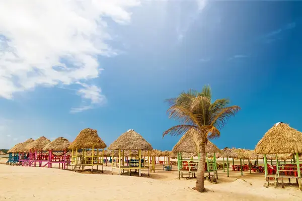 Barracas coloridas na Praia do Pesqueiro, na Ilha de Marajó, com areia clara e céu azul.