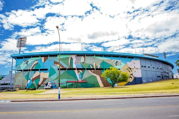 Vista externa do Estádio Centenário com um grande mural artístico colorido pintado em sua fachada.