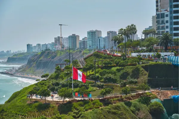 Bandeira do Peru tremulando no Parque del Amor, em Miraflores, com vista para o Oceano Pacífico e prédios modernos de Lima ao fundo.
