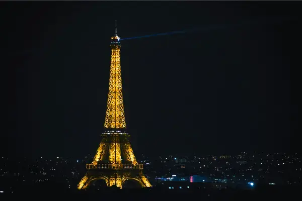 Torre Eiffel iluminada à noite com luzes douradas, vista panorâmica da cidade de Paris.