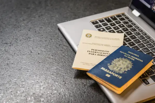passaporte brasileiro aberto ao lado da permissão internacional para dirigir, em cima de um notebook