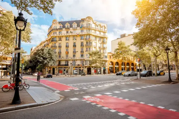 Rua em Barcelona com ciclovia vermelha em destaque, prédios históricos ao fundo e luz do sol iluminando a cena.