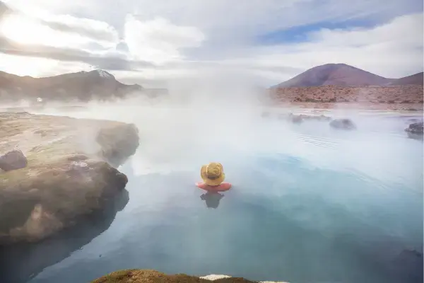 Viajante relaxando em terma natural com vapor e montanhas ao fundo no Chile