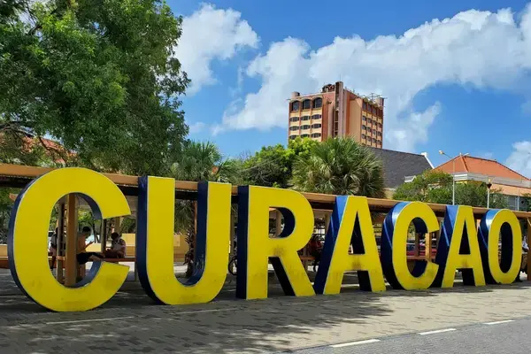 Letreiro amarelo com a palavra Curaçao em praça arborizada de Willemstad