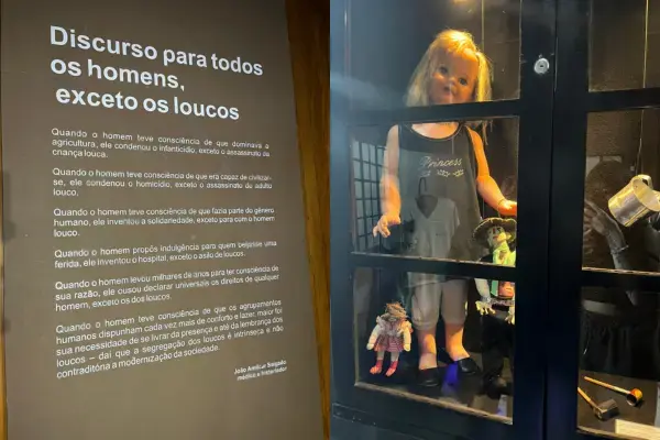 Exposição do Museu da Loucura em Barbacena com texto e bonecos em vitrine.