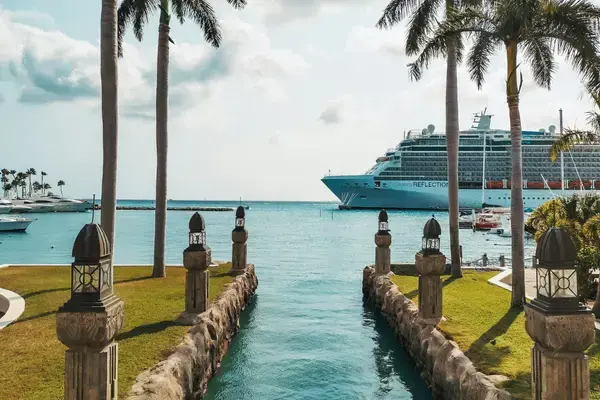 Navio de cruzeiro atracado no porto de águas turquesas em Aruba entre palmeiras.