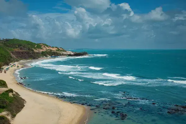 Vista panorâmica da Praia de Pipa com falésias, faixa de areia e ondas no litoral potiguar.