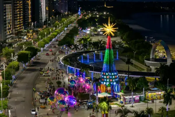 Orla da Ponta Negra em Manaus iluminada para o Natal com árvore colorida e visitantes caminhando à noite.
