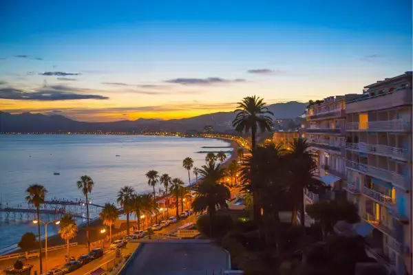 Vista da Croisette em Cannes ao pôr do sol, com palmeiras e o mar Mediterrâneo