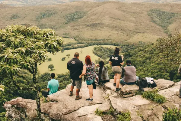 Grupo de trilheiros contemplando vale verde de mirante rochoso em São Tomé das Letras, MG