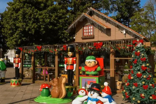 Cenário natalino em Canela com casinha decorada, soldadinhos, árvores enfeitadas e personagens infantis em área externa.
