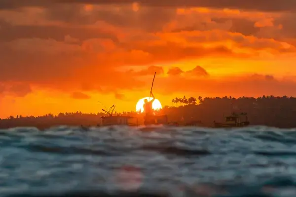 Pôr do sol dramático em Alagoas com silhueta de pescador e barcos no mar