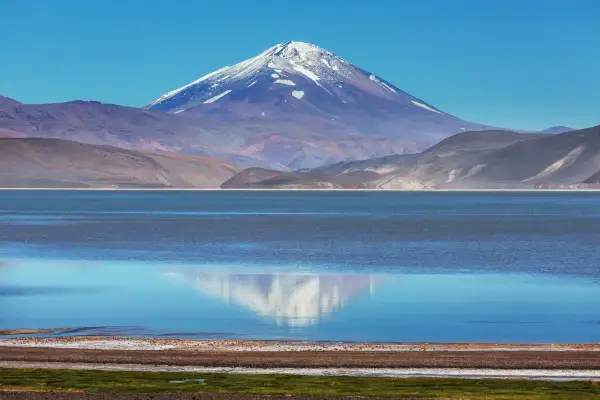 Vulcão com neve refletido em lagoa azul no altiplano do Chile