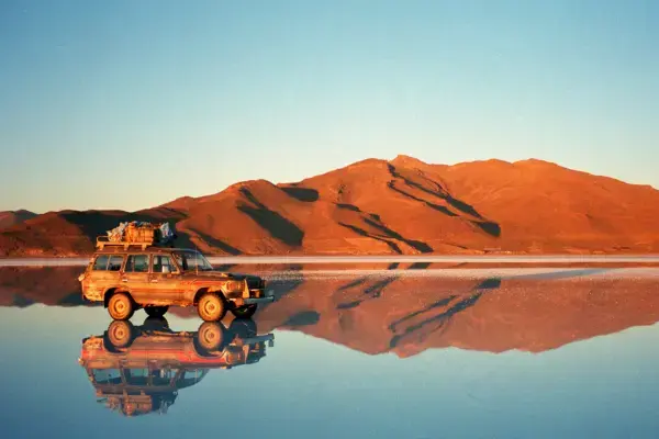 Veículo 4x4 refletido no efeito espelho do Salar de Uyuni ao pôr do sol