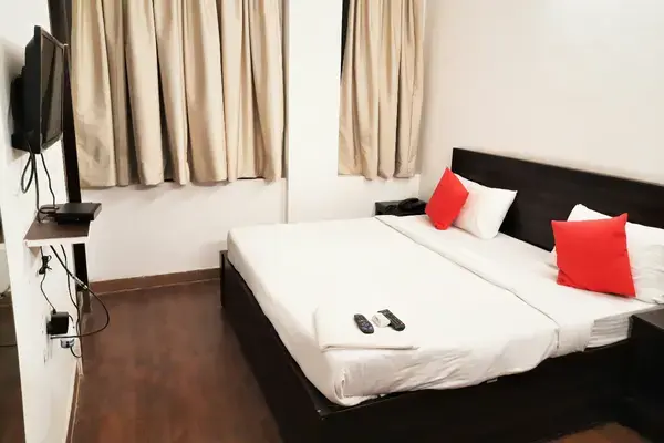 Quarto de hotel simples com cama de casal, piso de madeira e TV de parede em São Paulo.