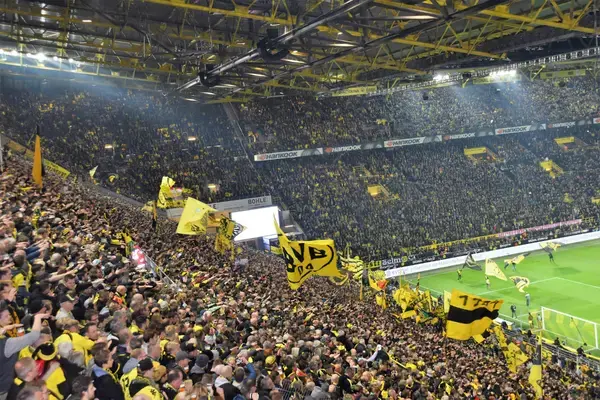 Torcida do Borussia Dortmund na Muralha Amarela do Signal Iduna Park, com arquibancada lotada de torcedores vestidos de amarelo e bandeiras do BVB durante partida.