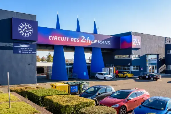Entrada principal do Circuit des 24 Heures du Mans com sinalização oficial do evento e carros estacionados em frente ao complexo.