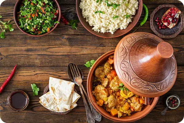 Tagine marroquino de frango sendo servido em sua panela de barro tradicional, com pedaços de frango, damascos e azeitonas visíveis.